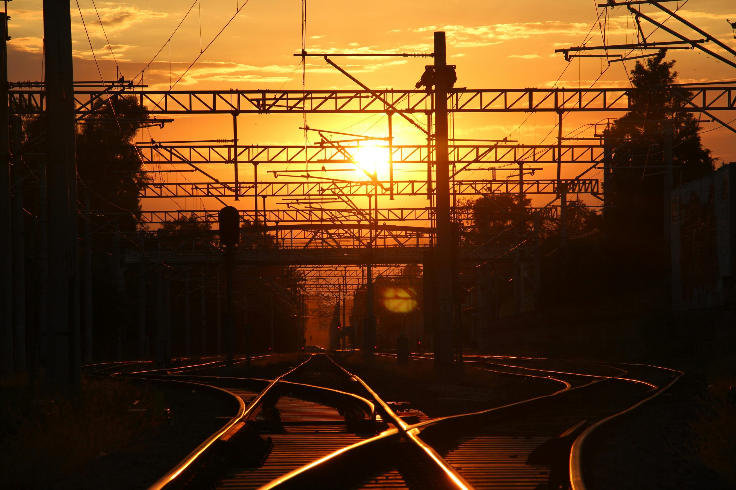 Silhouetted railroad tracks and utility poles against a vivid sunset sky.