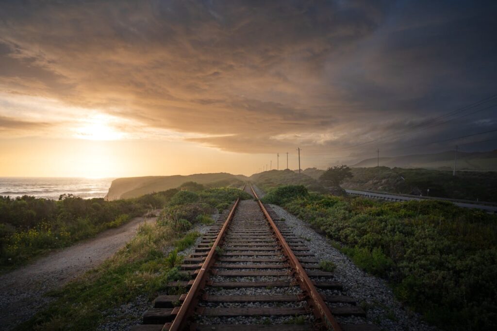 Sunset view of railroad tracks along a scenic coastline under a dramatic cloudy sky.