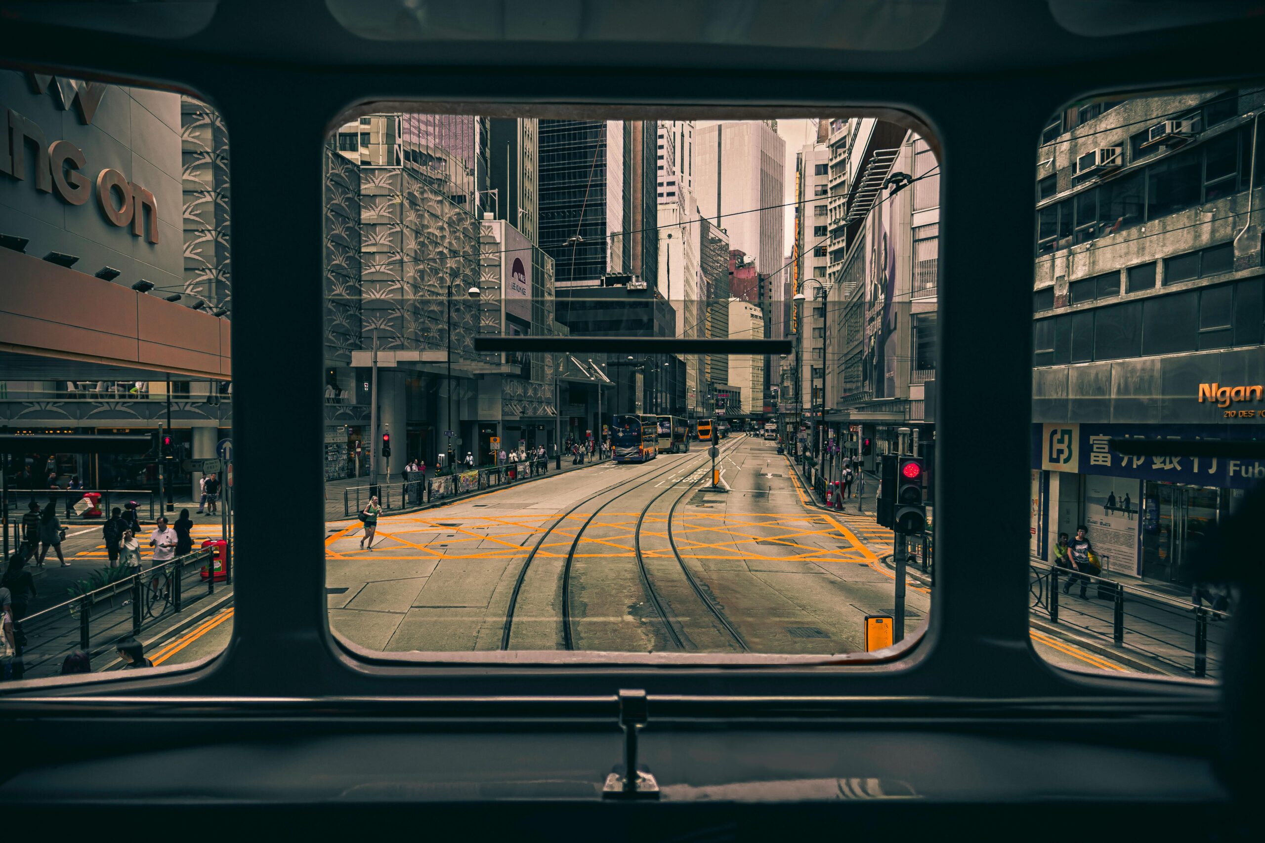 A bustling Hong Kong street seen through a tram window, featuring skyscrapers and public transport.