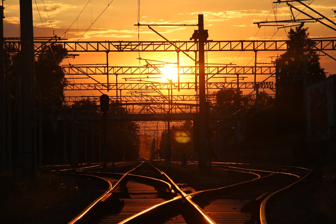 Silhouetted railroad tracks and utility poles against a vivid sunset sky.